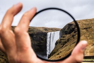 perspective: hand holding a magnifying lens and focusing on a waterfall