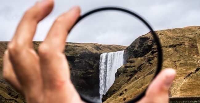 perspective: hand holding a magnifying lens and focusing on a waterfall
