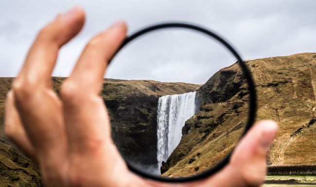 perspective: hand holding a magnifying lens and focusing on a waterfall